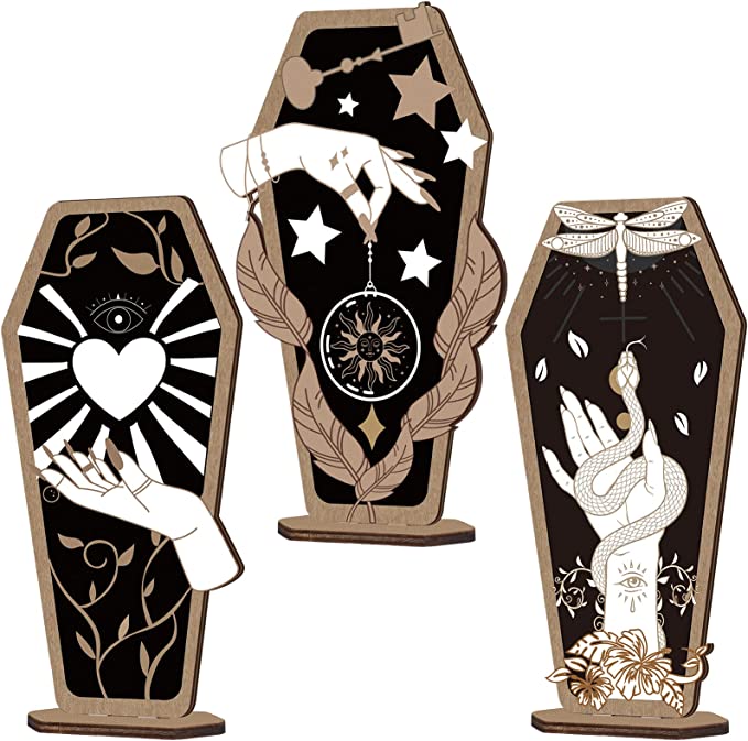 Halloween decor idea: 3 wooden coffin standees that depict different hand illustrations. One is a hand with a floating heart above it. One is holding a dream catcher and the other is holding a snake and there is a dragon fly above it.