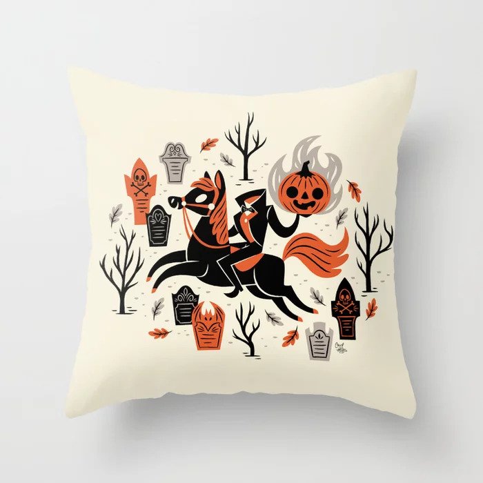 Picture of a throw pillow with an illustration of a headless horseman on horse back holding up his pumpkin head. He's surrounded by dead trees and tombstones.