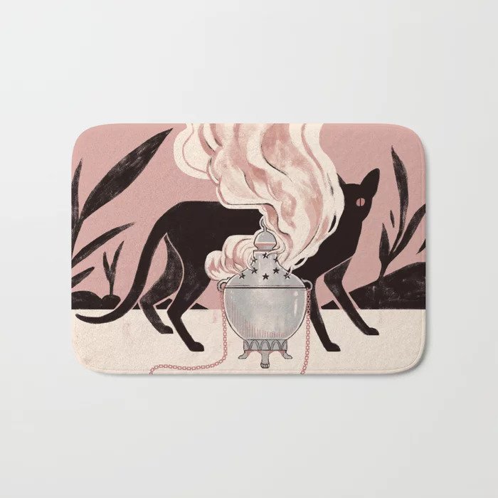 A bath mat with a pink, black and cream illustration of a black cat behind an incense decanter with smoke rising up.